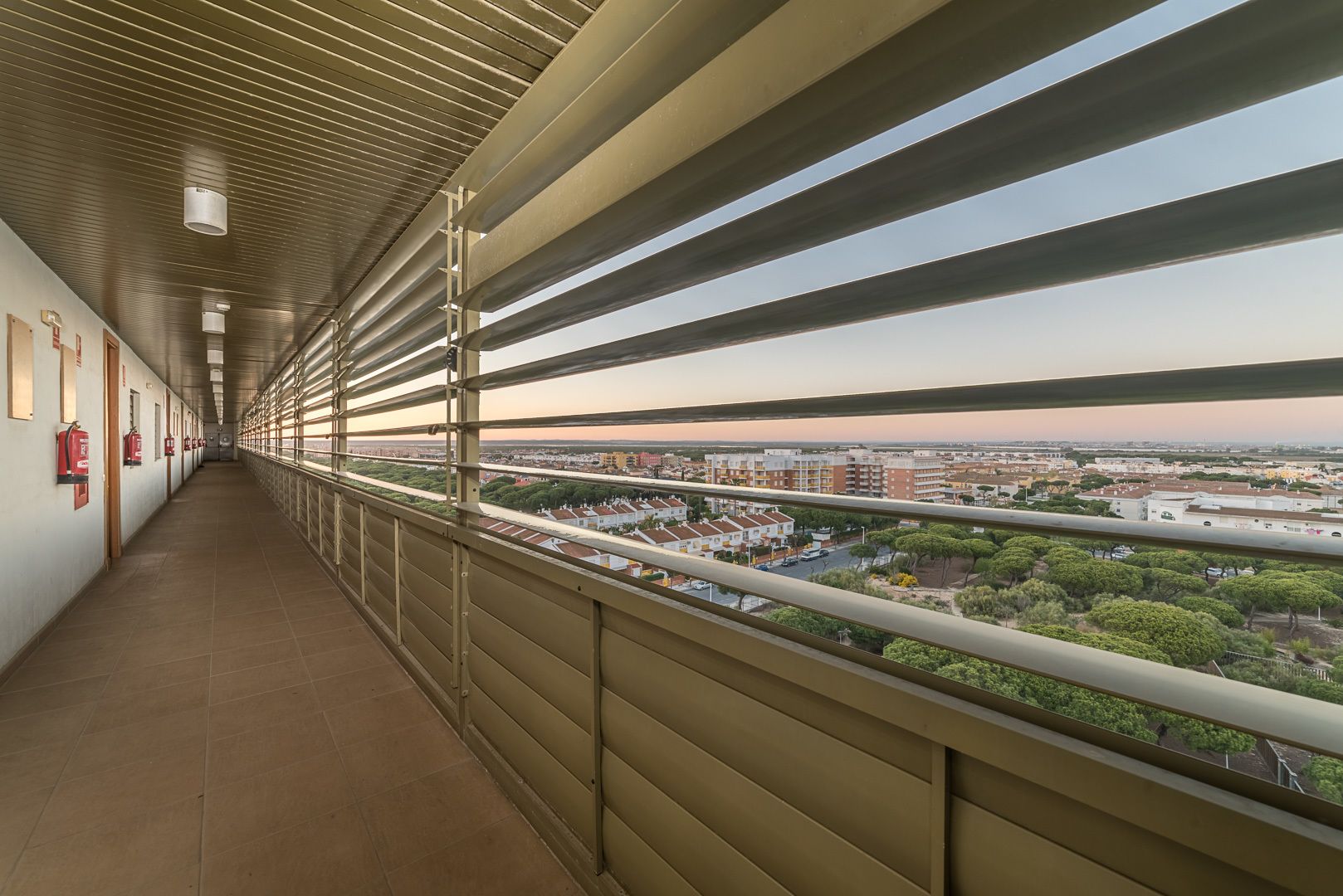 A corridor with a metal railing and a view of a residential area.