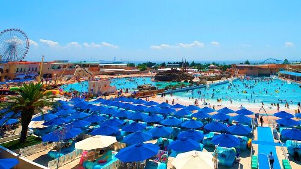 A large outdoor swimming pool with numerous blue umbrellas, a Ferris wheel, and a clear blue sky. - Nishiura Onsen Hotel Tokaien (Gamagori)