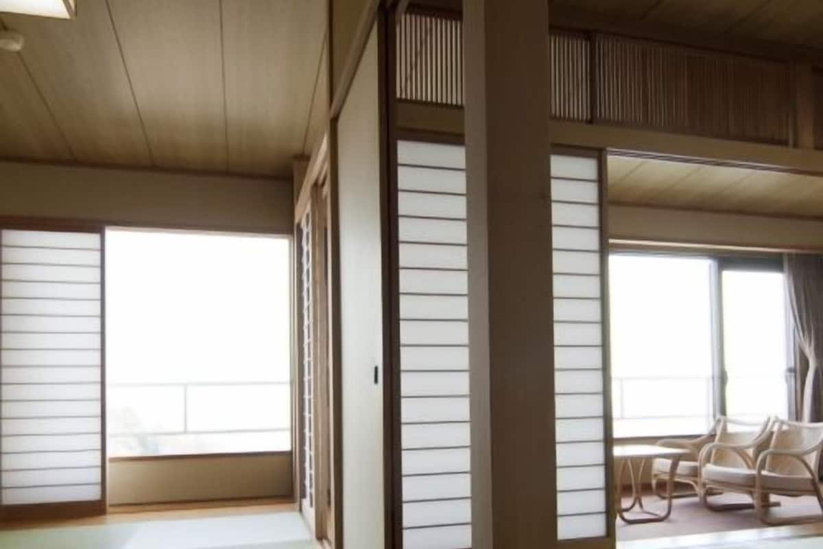 A traditional Japanese room with tatami flooring, sliding doors, and a view of the outside.
