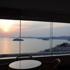 A room with a large window overlooking a body of water and distant landforms. - Nishiura Onsen Hotel Tokaien (Gamagori)