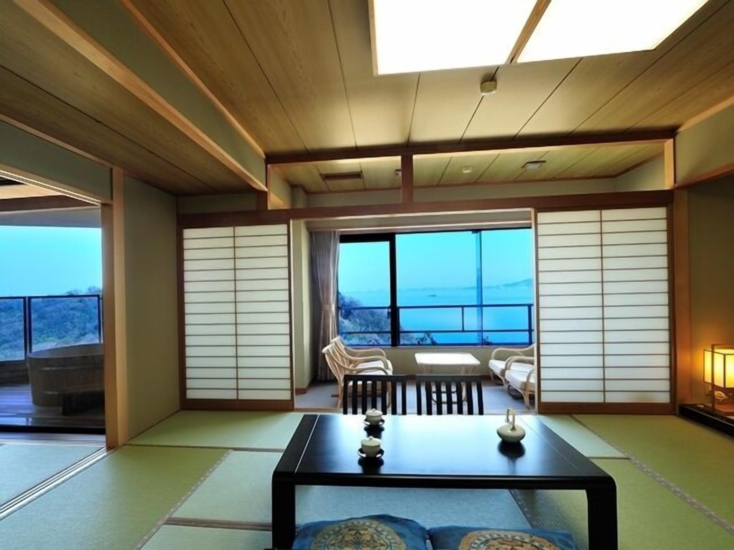 Una habitación tradicional japonesa con suelo de tatami, una mesa baja con juego de té y vista al mar a través de grandes ventanales.
