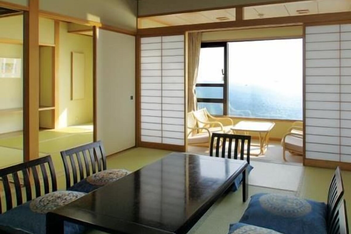 A traditional Japanese room with tatami flooring, a low table with chairs, and a sliding shoji screen door.