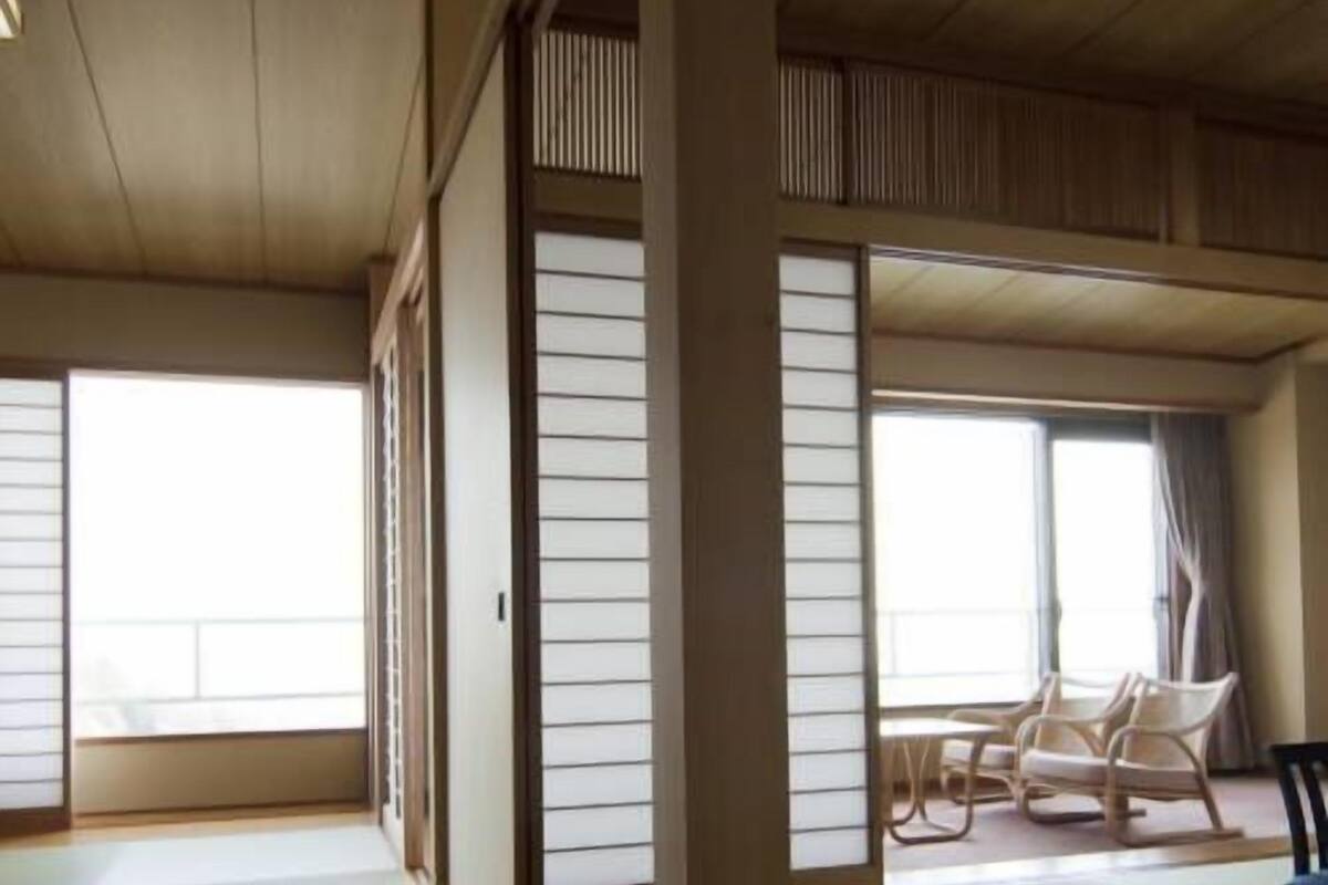A traditional Japanese room with tatami flooring, sliding doors, and a seating area with chairs.