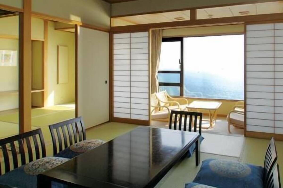 A traditional Japanese room with tatami flooring, a low table with chairs, and a sliding shoji screen door.