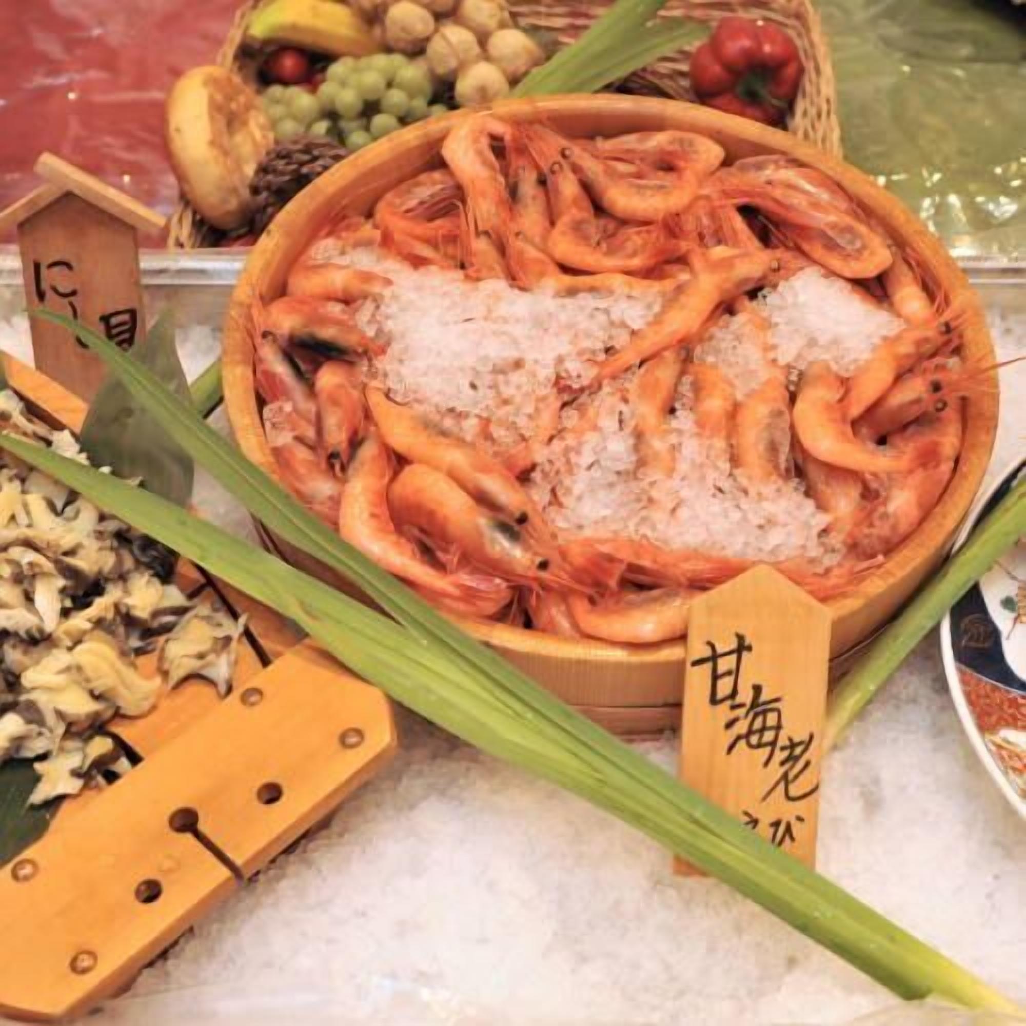 A bowl of shrimp on ice with a wooden sign, surrounded by various food items.
