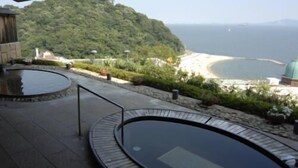 A pool area with a view of a beach and a forested hill. - Nishiura Onsen Hotel Tokaien (Gamagori)