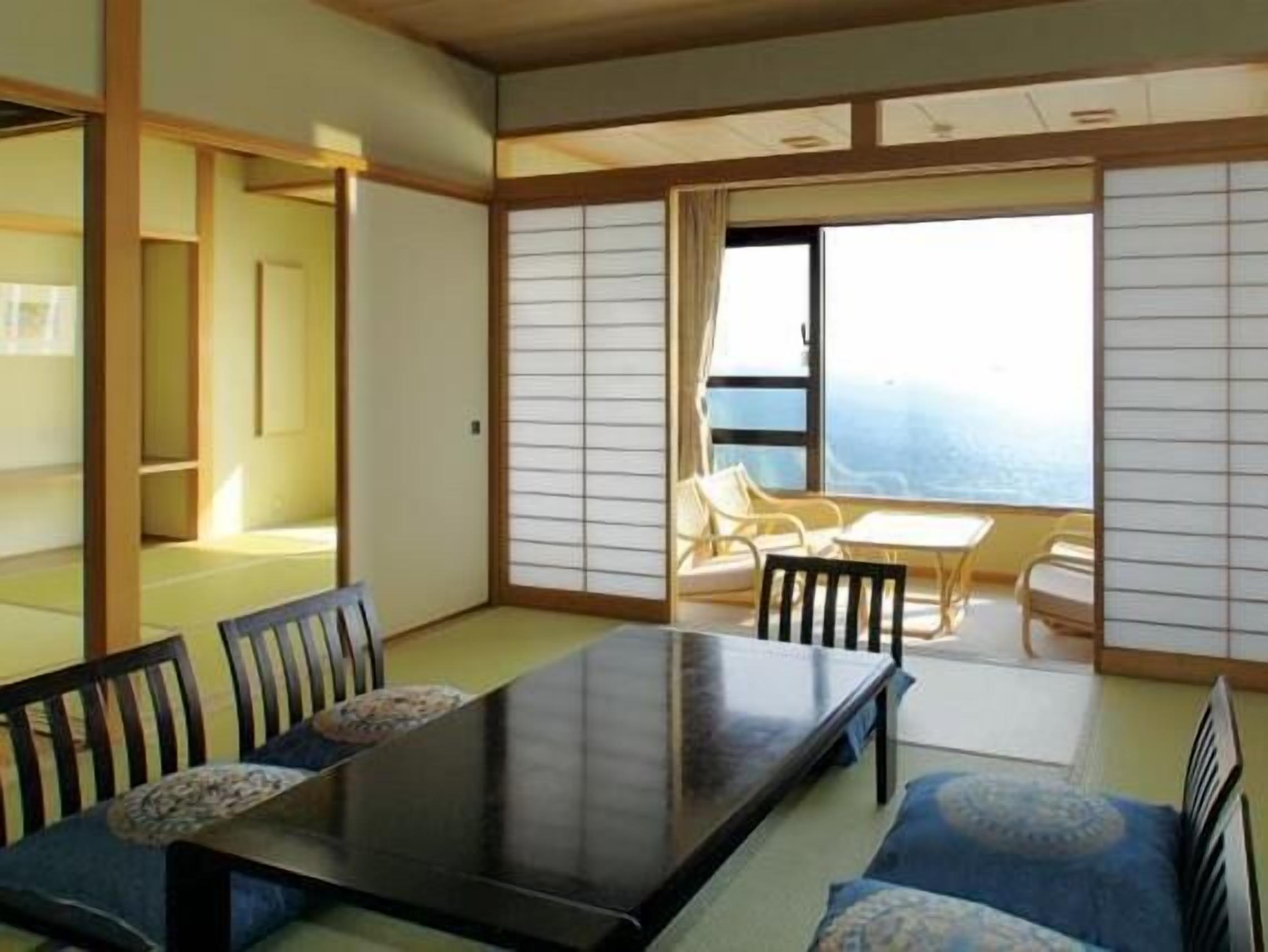Una habitación tradicional japonesa con suelo de tatami, una mesa baja con sillas y una puerta corredera tipo shoji.