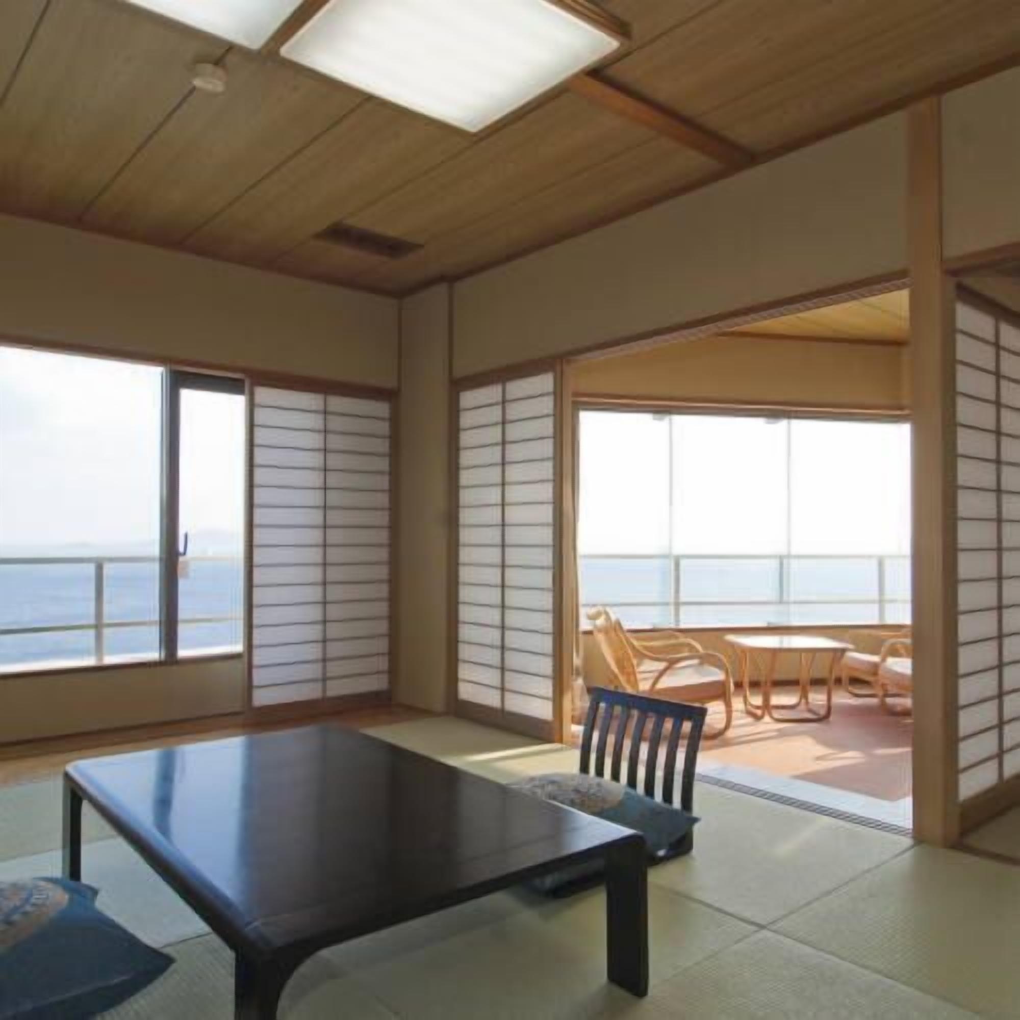 Una habitación con suelo de tatami, una mesa baja y puertas correderas que dan a un balcón con vistas al mar.