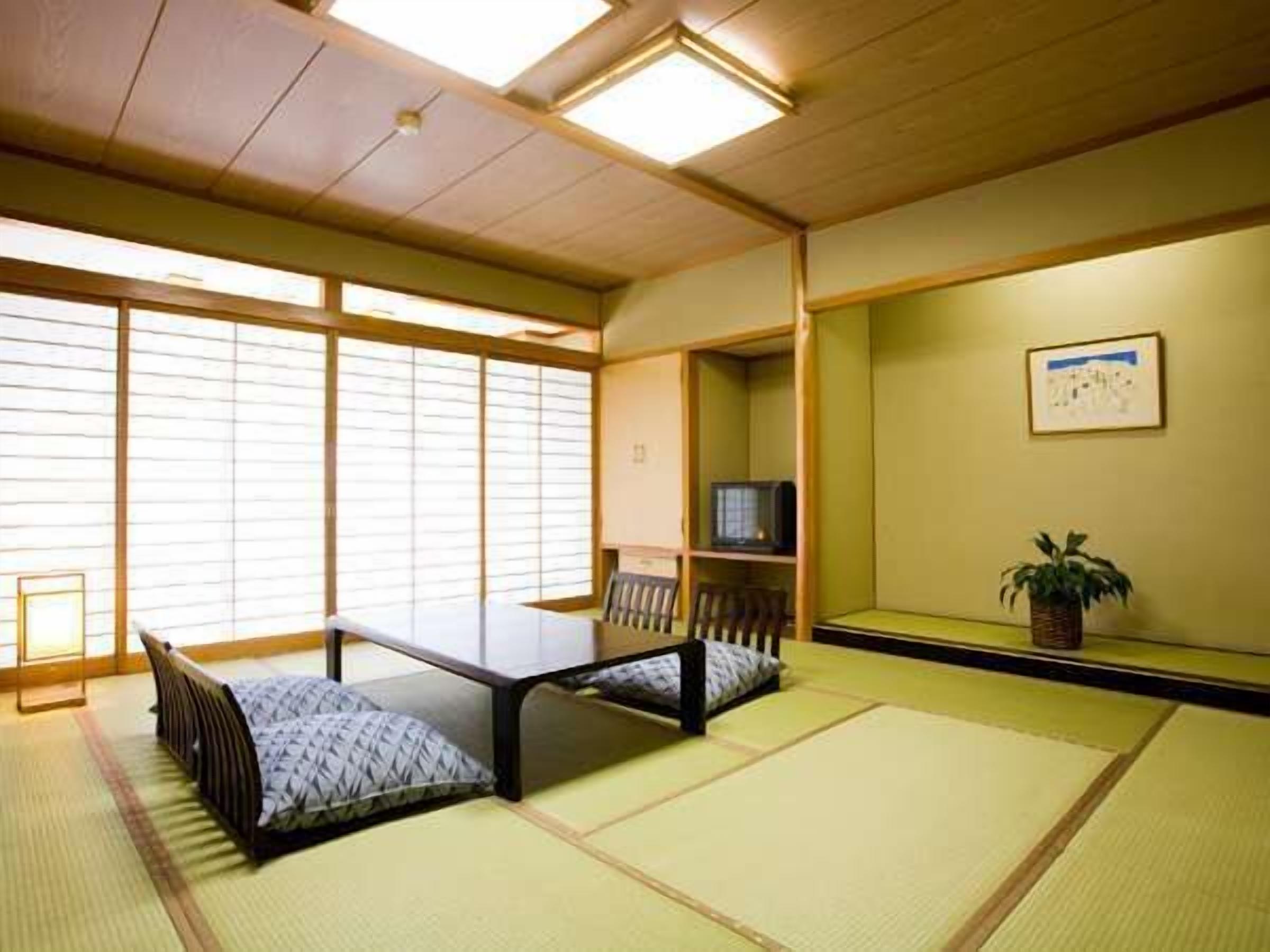 A tatami mat room with a low table, a TV on a shelf, and a plant on the wall.