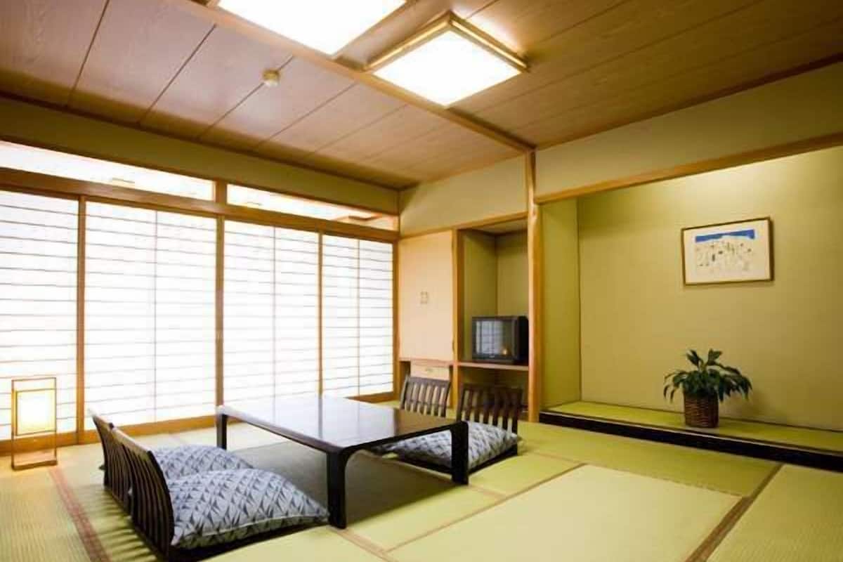 A tatami mat room with a low table, a TV on a shelf, and a plant on the wall.