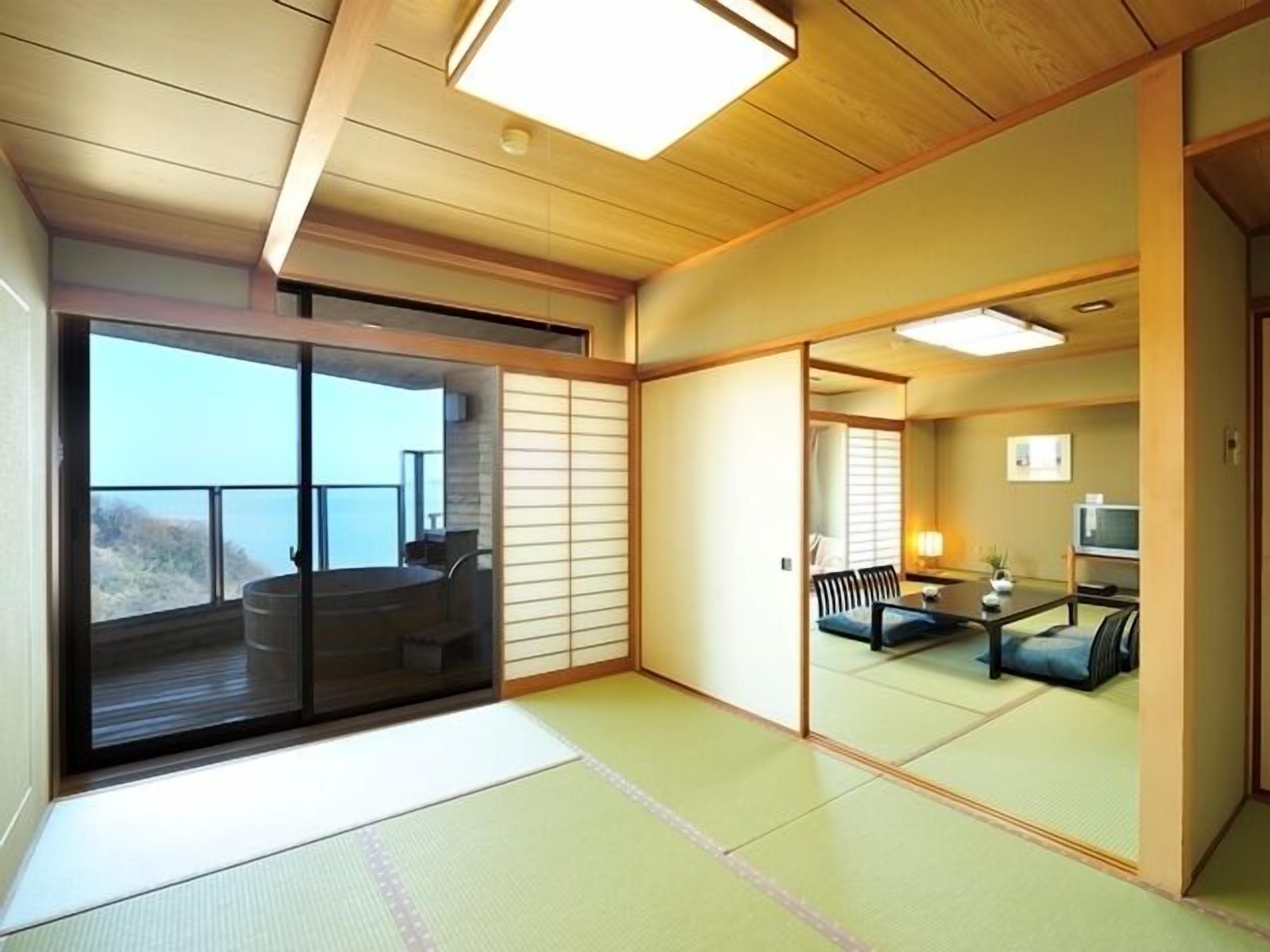 Una habitación japonesa tradicional con suelo de tatami, puertas correderas, un balcón con vistas y una pequeña zona de estar con mesa y sillas.