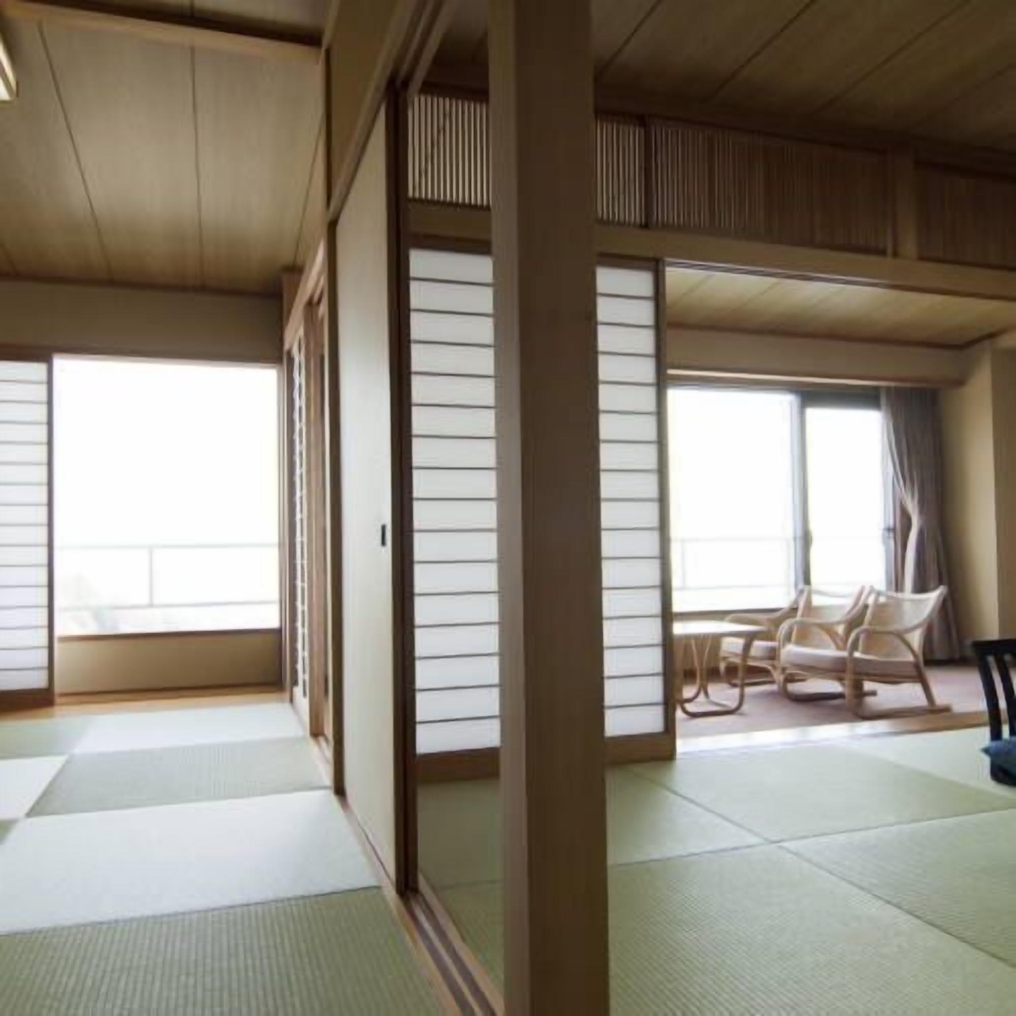 Una habitación japonesa tradicional con suelo de tatami, puertas correderas shoji y una zona de estar con sillas.
