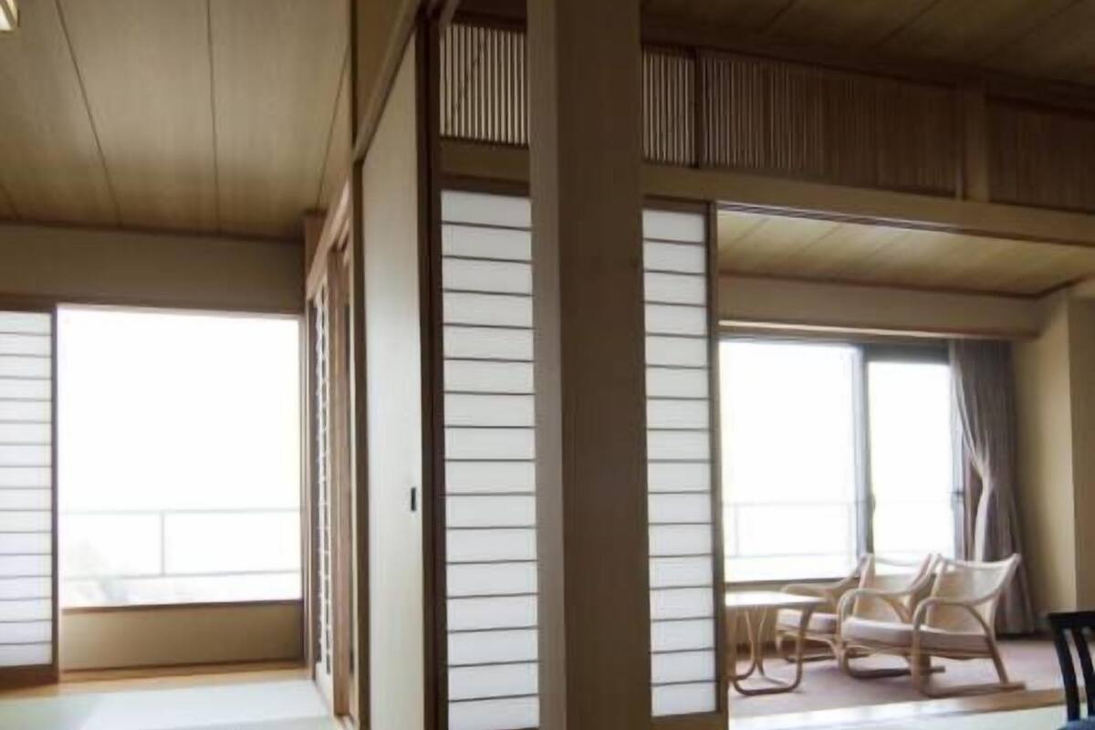 A traditional Japanese room with tatami flooring, sliding shoji doors, and a seating area with chairs.