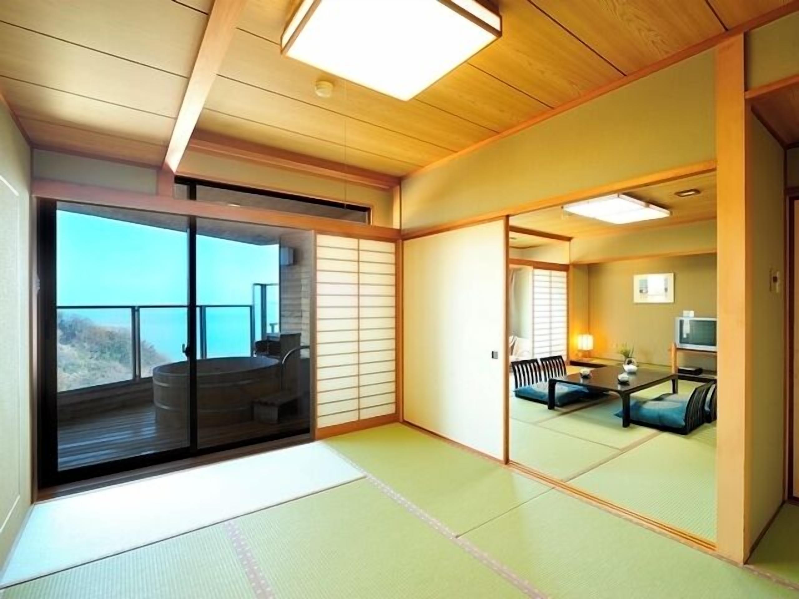 A traditional Japanese room with tatami flooring, a sliding door, a balcony with a view, and a small seating area with cushions.