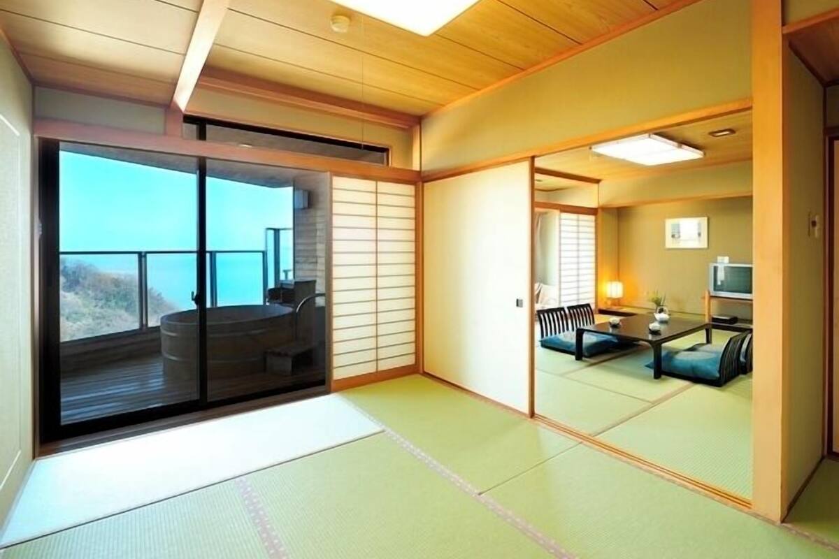 A traditional Japanese room with tatami flooring, a sliding door, a balcony with a view, and a small seating area with cushions.
