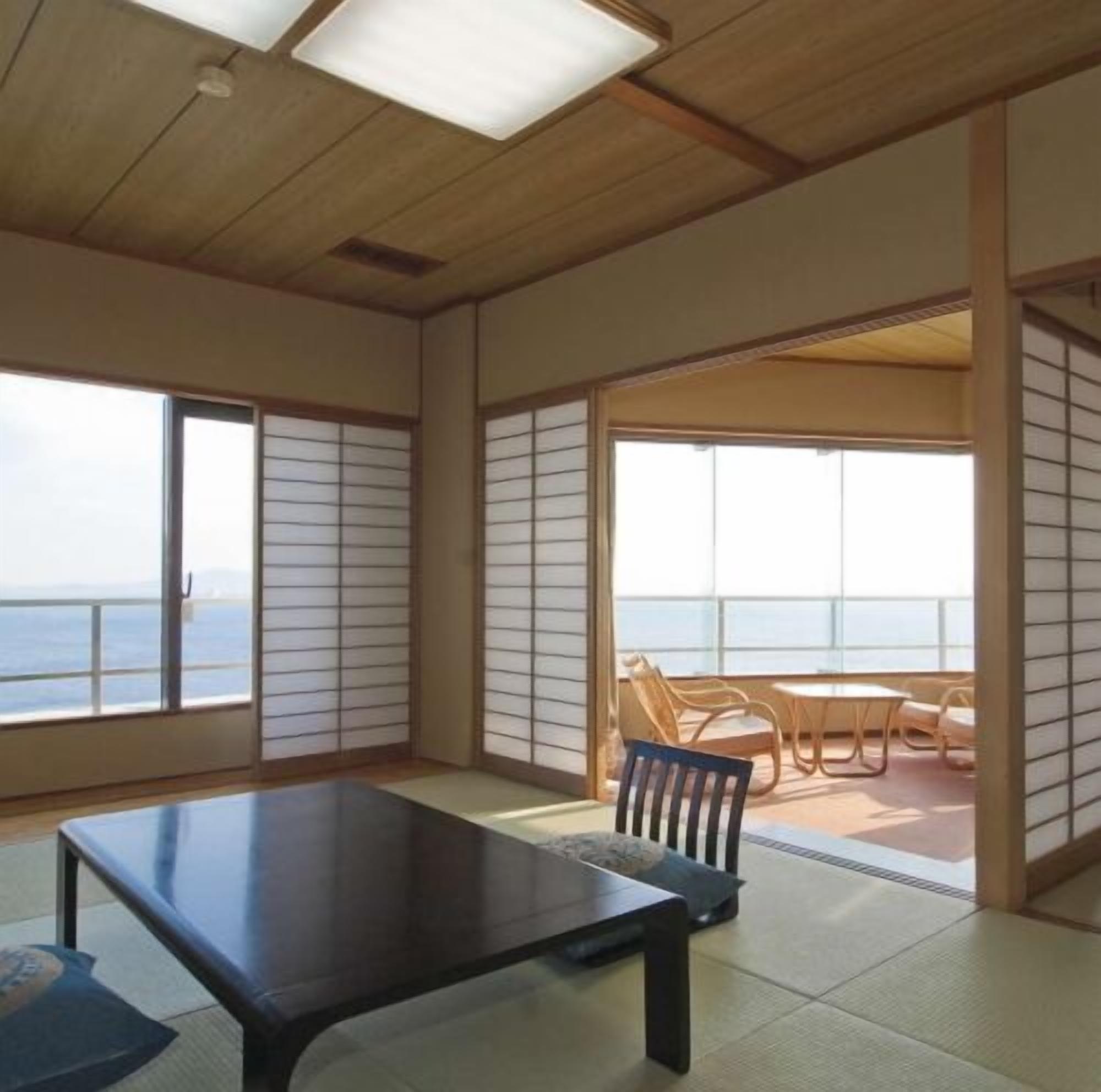 A room with tatami flooring, a sliding door leading to a balcony with a view of the sea, and a table with chairs.