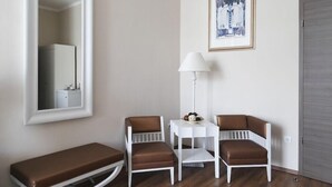 Una habitación pequeña y luminosa con un banco, dos sillas, una mesa, una lámpara y un cuadro en la pared.