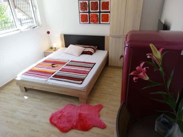A bedroom with a bed, a red refrigerator, a pink rug, and a wall with spice pictures.