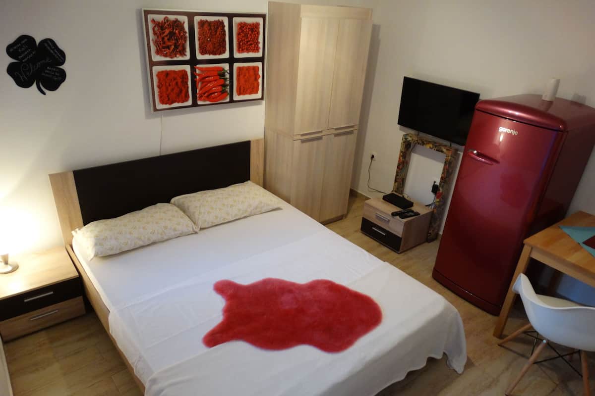 Une chambre à coucher avec un lit, une armoire, une télévision et un réfrigérateur rouge.