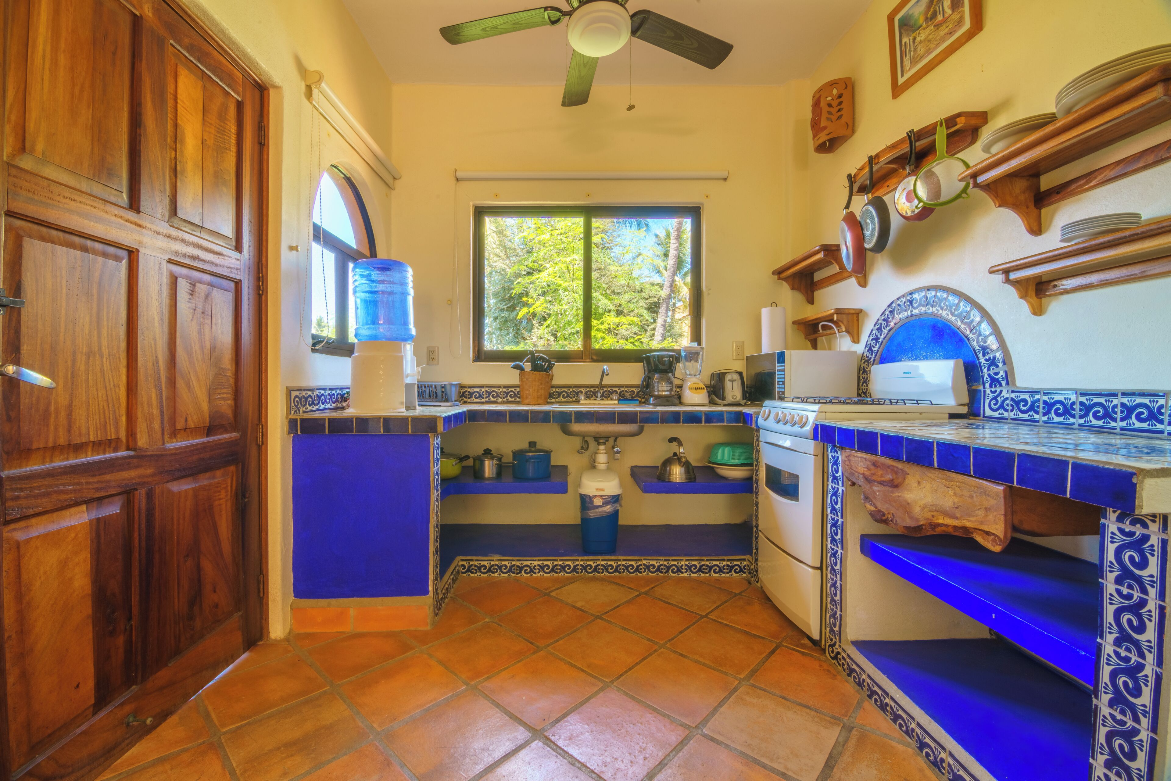 Une cuisine avec une fenêtre, des meubles en bois, une cuisinière et des plans de travail recouverts de carreaux bleus.