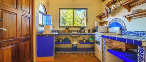 Une cuisine avec une fenêtre, des meubles en bois, une cuisinière et des plans de travail recouverts de carreaux bleus.