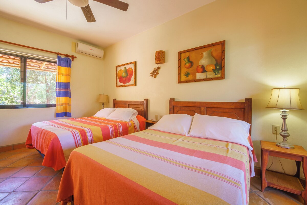 Habitación de hotel con dos camas, una ventana con cortina, una obra de arte en la pared y un ventilador de techo.