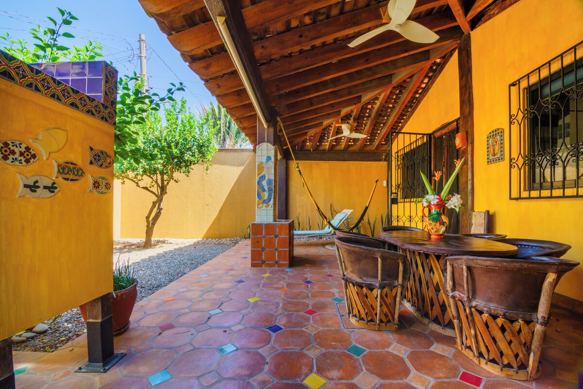 Un patio techado con suelo de baldosas, mobiliario de madera y un ventilador de techo.