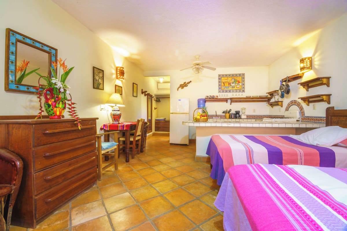 Habitación de hotel compacta con kitchenette, comedor, cama con ropa de cama a rayas y cómoda de madera.