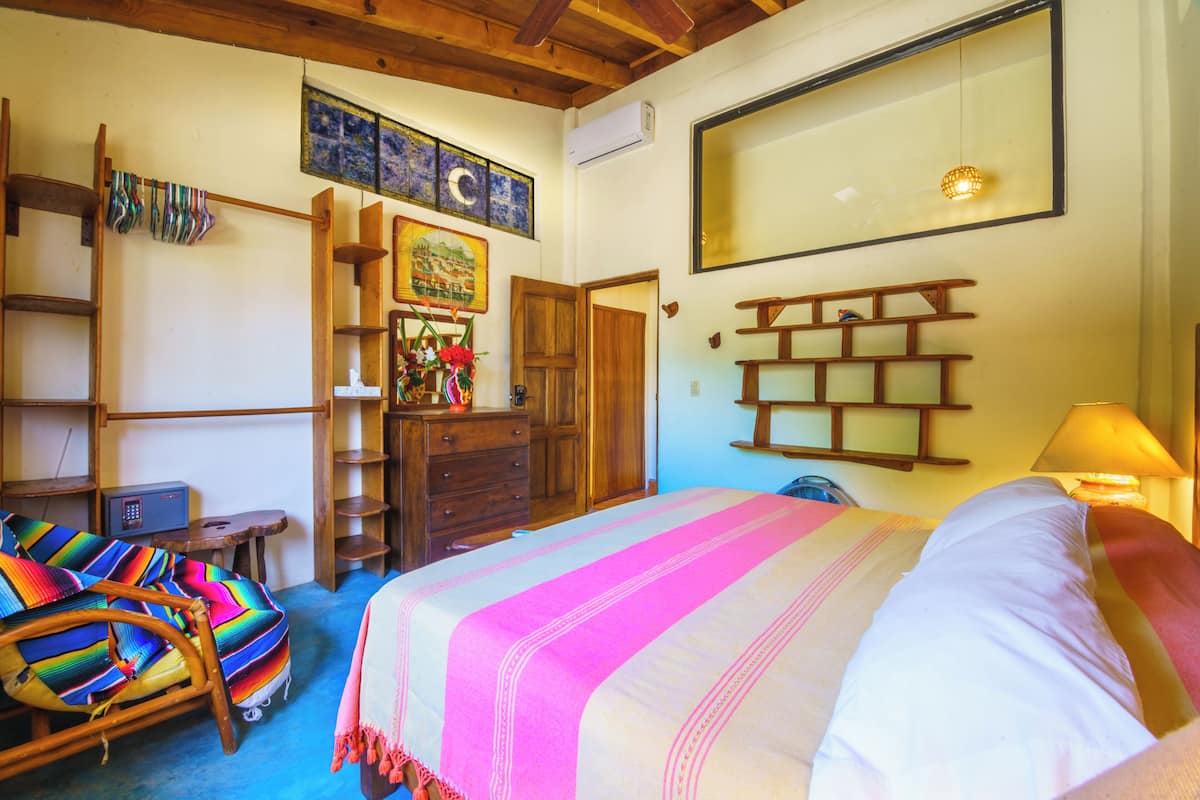 Una habitación con cama, una silla, cómoda, estante y una lámpara de pared.