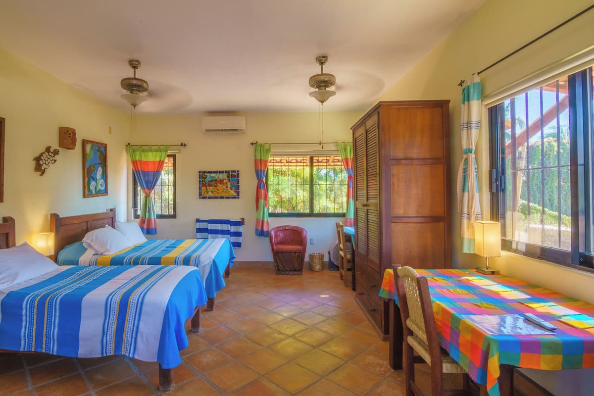 Habitación de hotel con dos camas, una mesa de comedor, una silla, un ventilador y una ventana con cortinas.