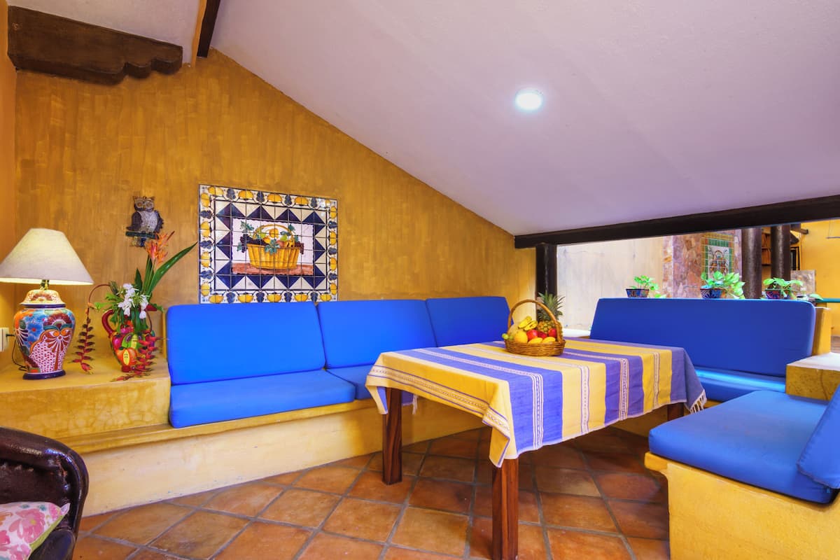 Una habitación acogedora con un sofá azul, una mesita con mantel a rayas, una lámpara decorativa y una pared de azulejos con un diseño de cesta de frutas.