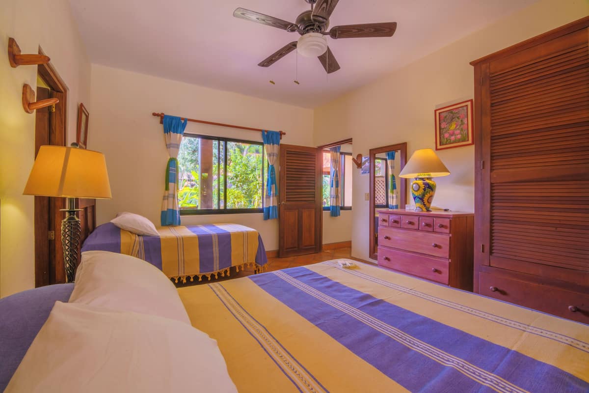 Un dormitorio con cama, cómoda, ventilador de techo y ventana con cortinas.