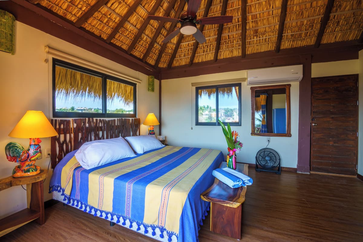 Una habitación con una cama, dos ventanas, un ventilador de techo y una puerta de madera.