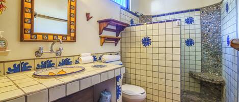 A bathroom with a sink, mirror, toilet, and shower area.