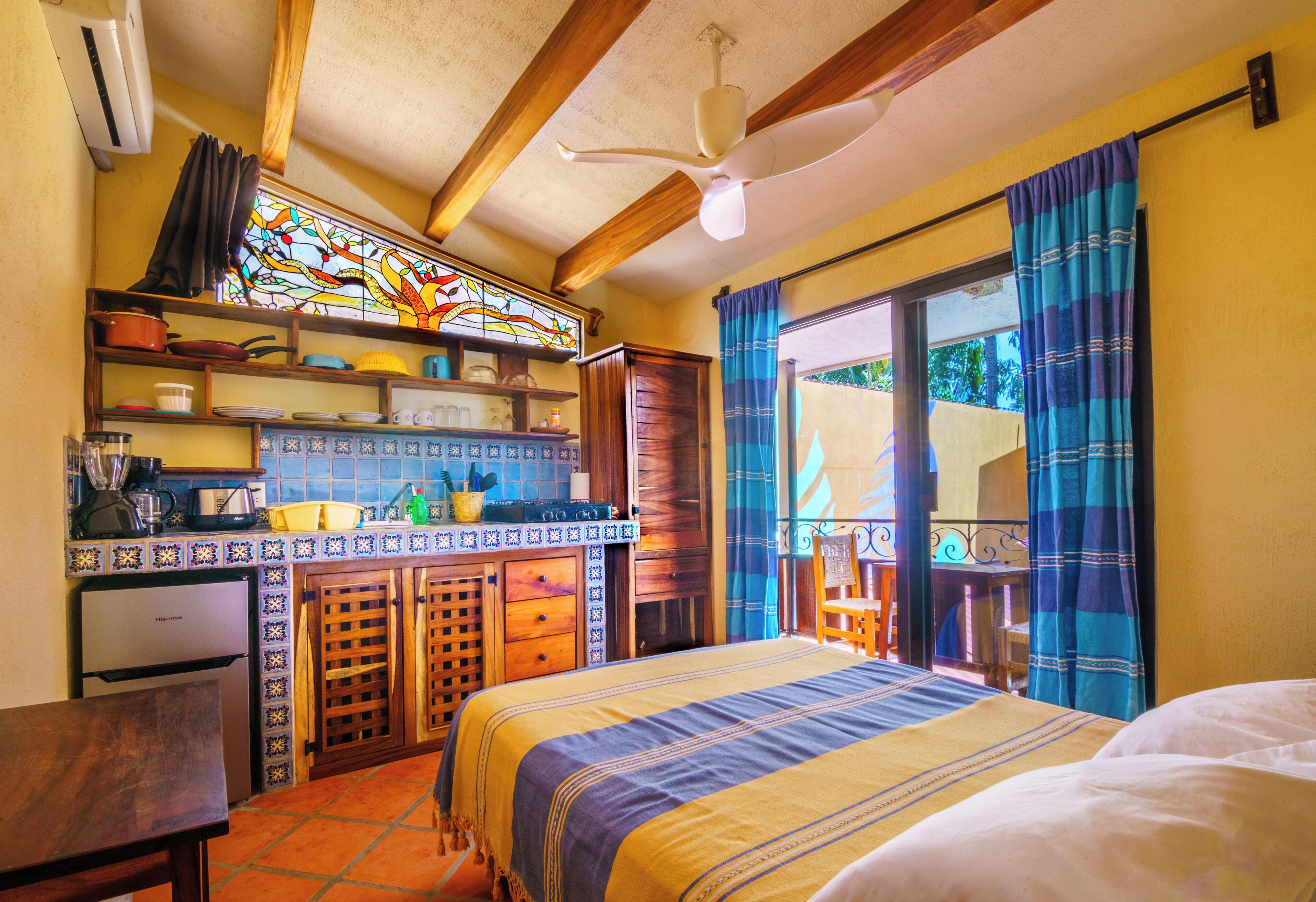 A compact room with a bed, a small kitchenette, a dining table, and a window with curtains.