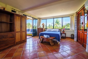 A bedroom with a bed, wooden wardrobe, and a view of palm trees.