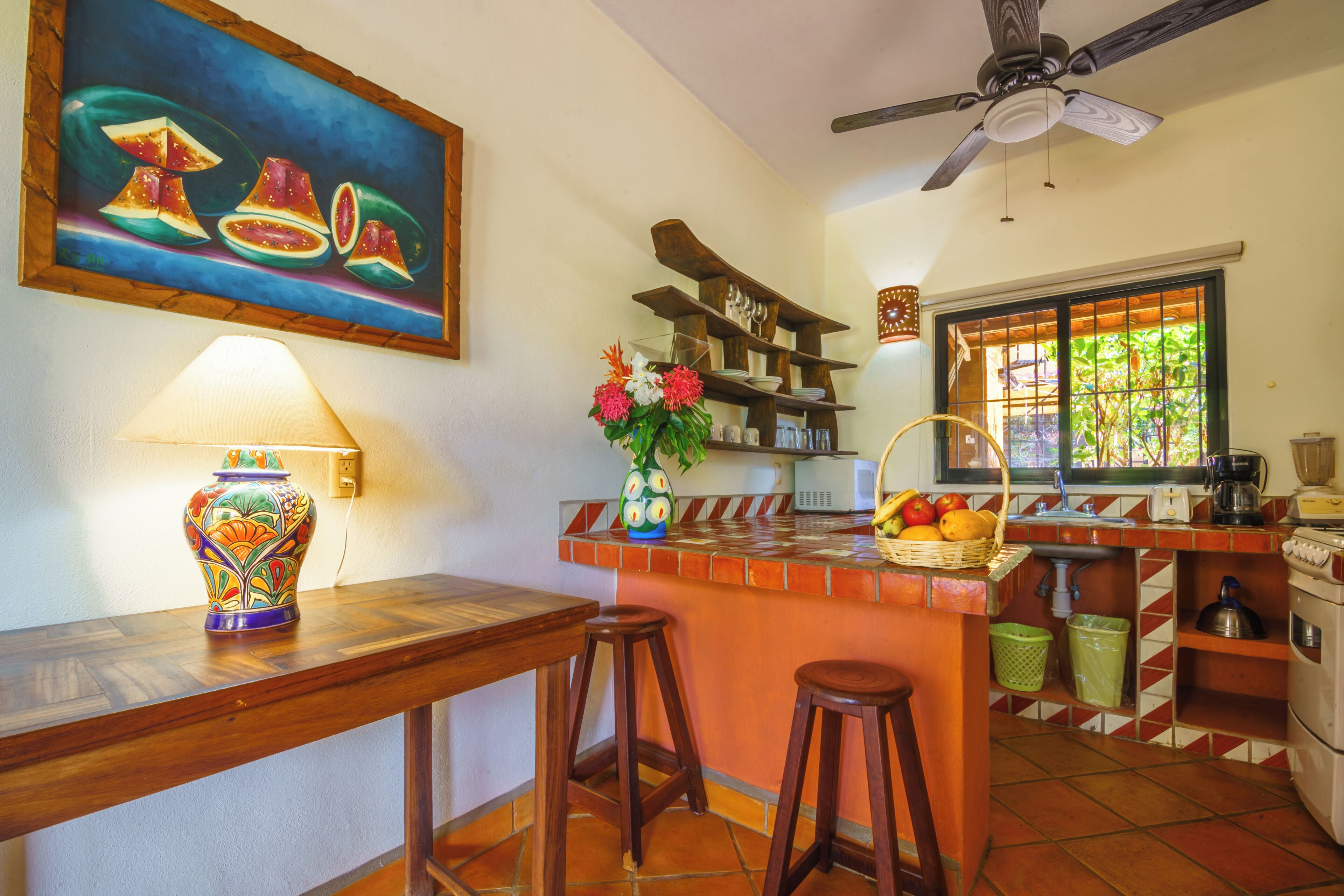 A kitchen with a wooden island, stools, a fruit basket, a microwave, and a window with a view.