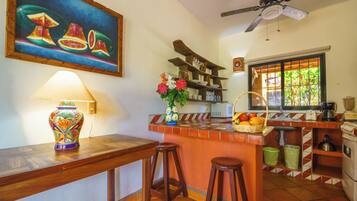 A kitchen with a wooden island, stools, a fruit basket, a microwave, and a window with a view.