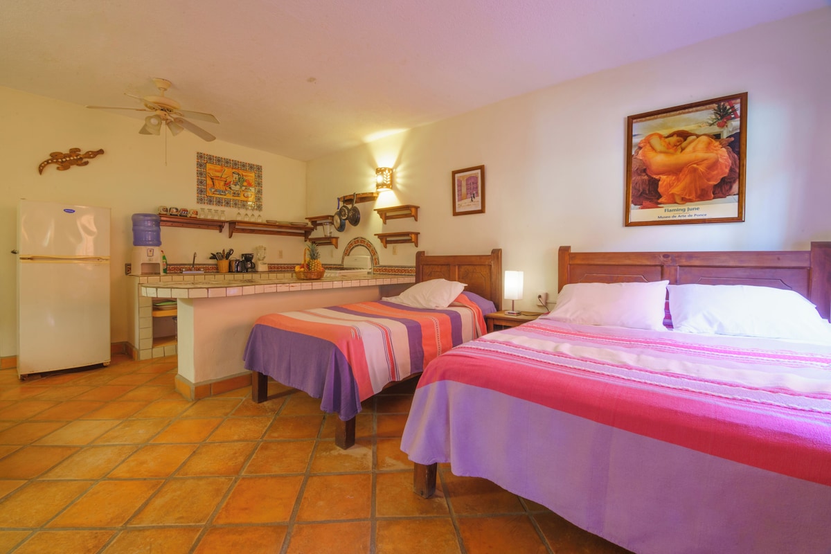 Una habitación con dos camas, una kitchenette y un ventilador de techo.