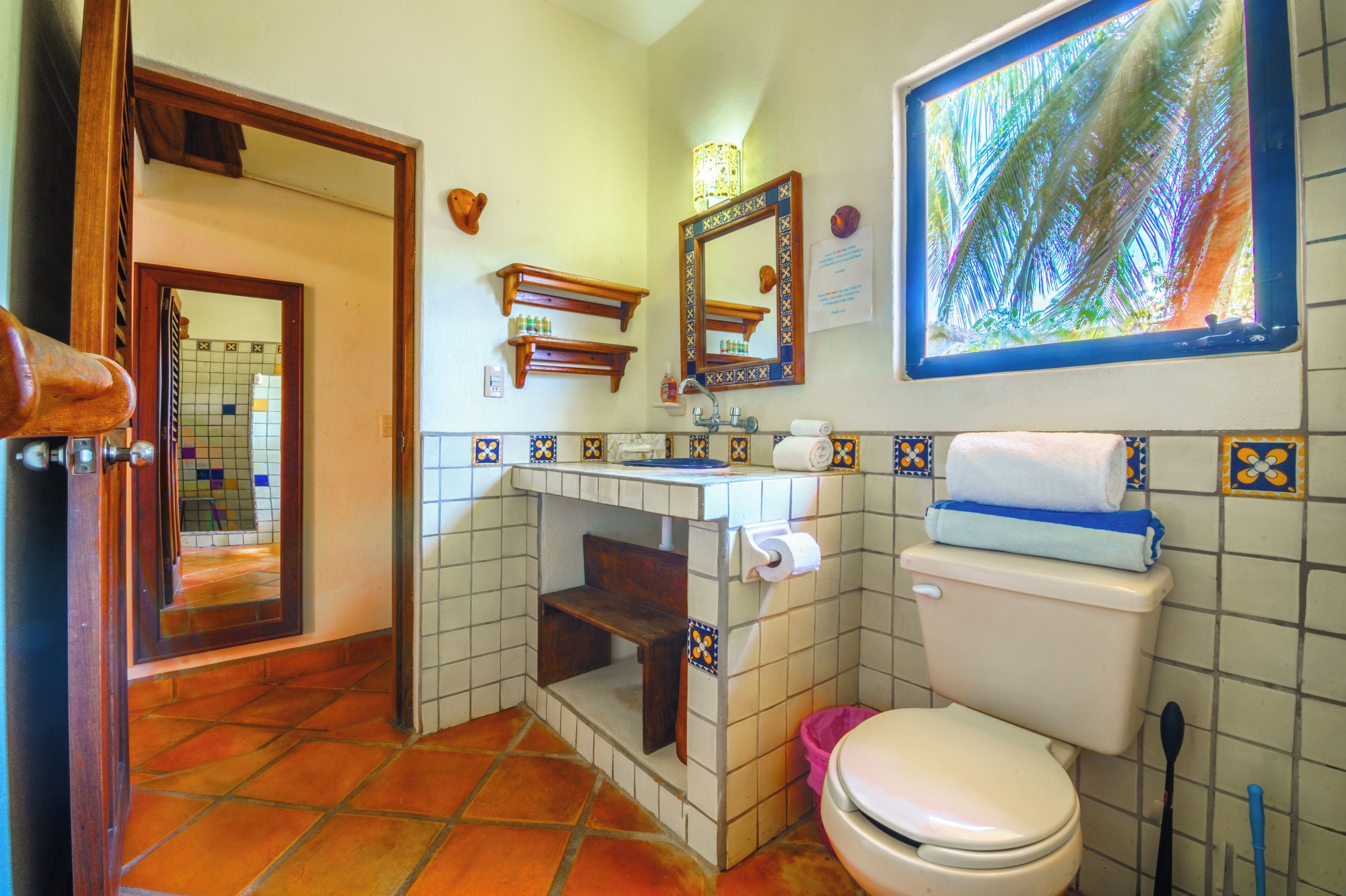 A bathroom with a toilet, sink, mirror, and tiled walls.