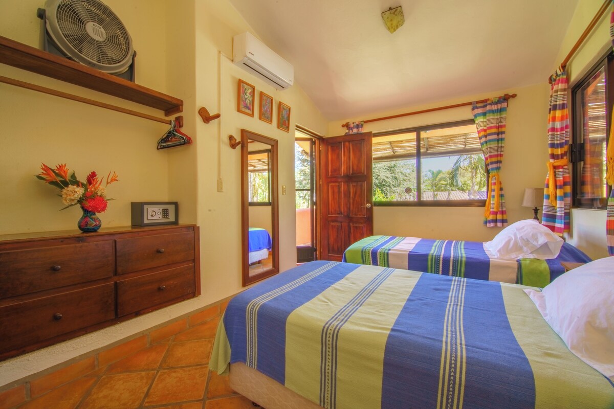 Una habitación con dos camas, un aparador, un ventilador, aire acondicionado y una ventana con cortinas.