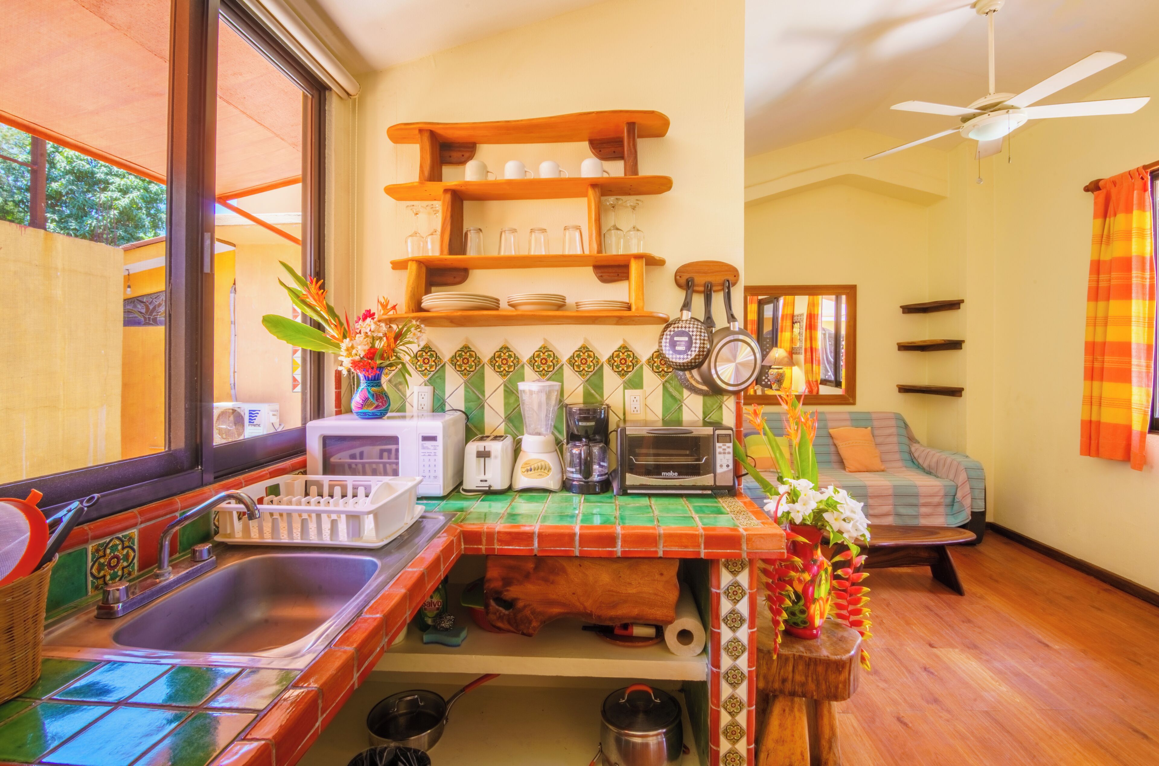 A kitchen with a sink, a toaster, a coffee maker, and a microwave. There is a window with a view of trees.