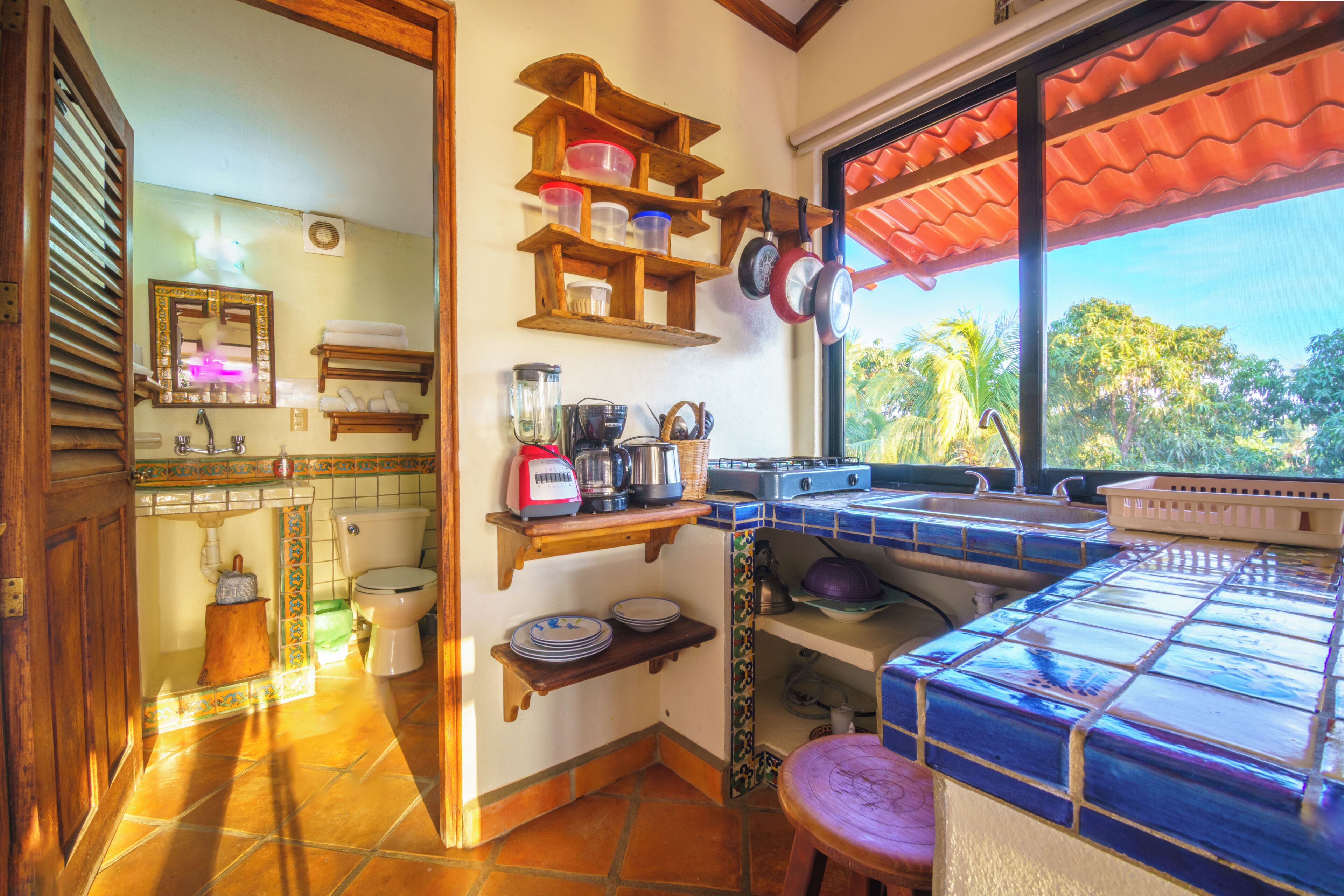 A kitchen with a tiled backsplash, wooden shelves, and a window with a view of greenery.