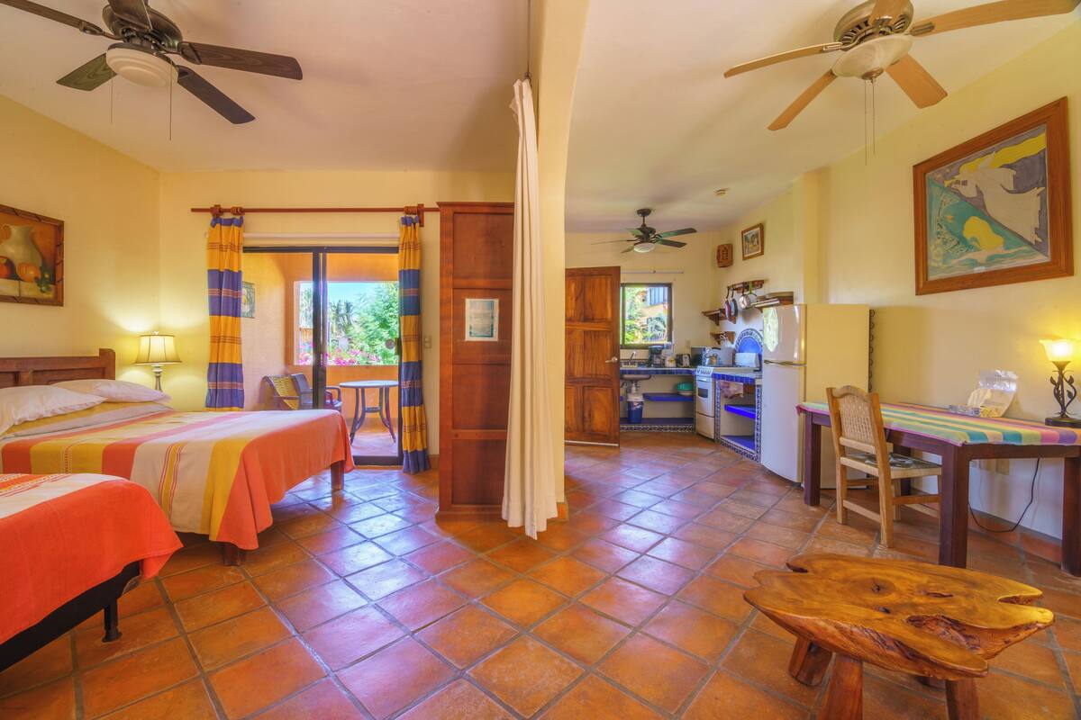 Una habitación con dos camas, una mesa de comedor, una mesa de centro de madera y una zona de cocina.