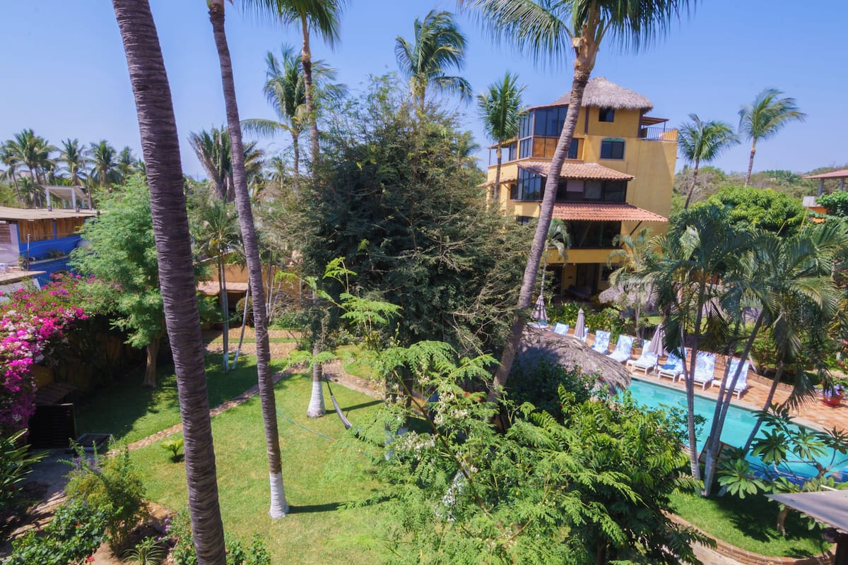 Un edificio de varios pisos con piscina, rodeado de palmeras y vegetación exuberante.