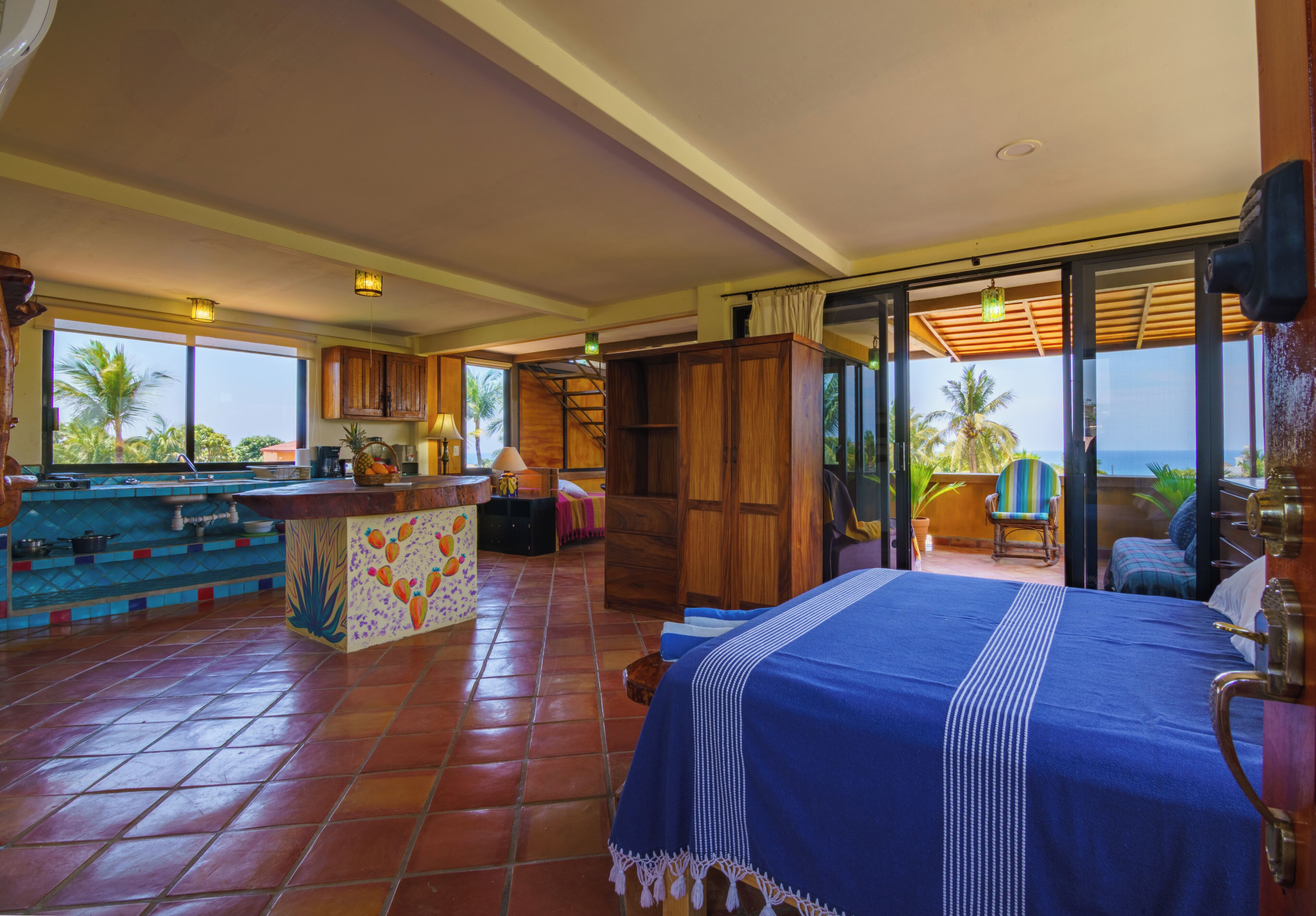 A spacious room with a large bed, a kitchen area, and a balcony with a view.
