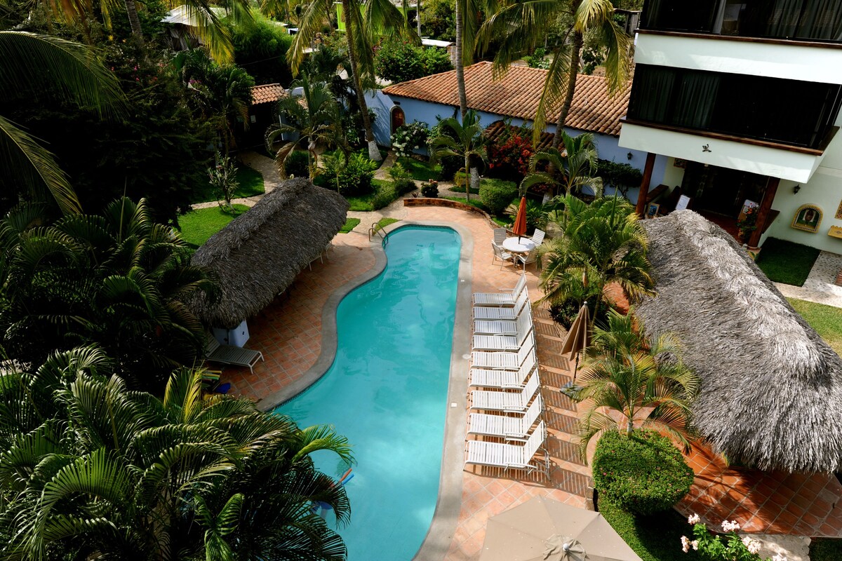 Un resort con piscina, sillas de descanso y construcciones de techo de paja.