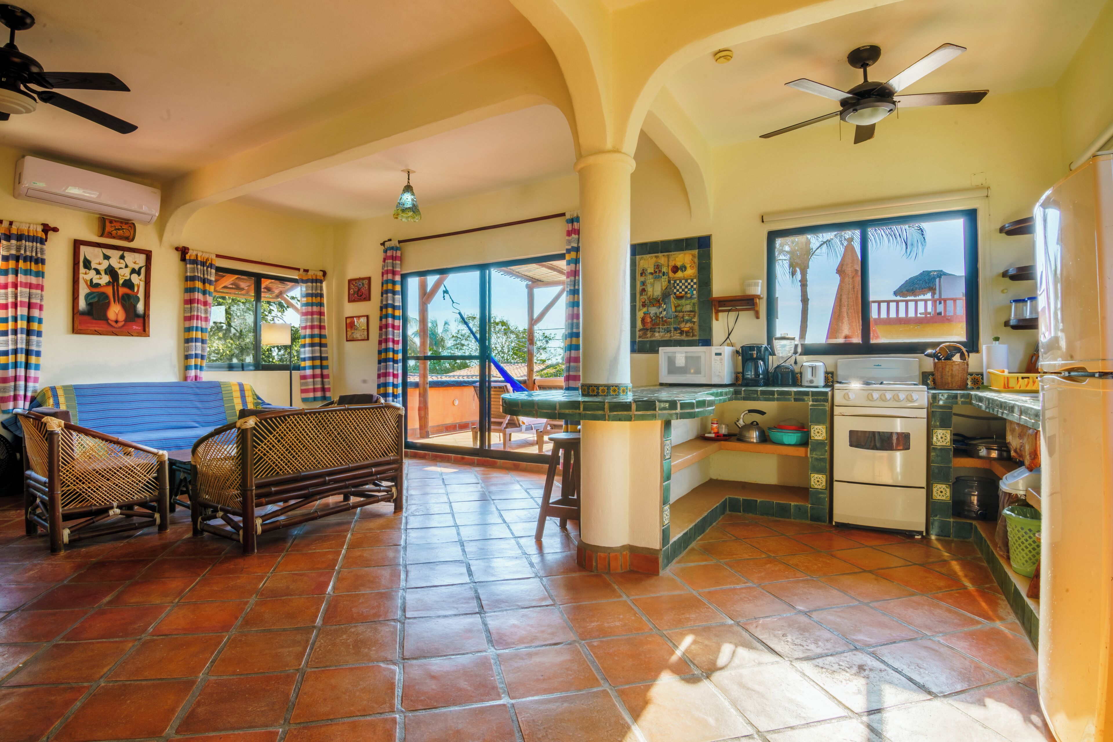 Un área de estar amplia con una mesa de comedor, sillas, un sofá, una cocina con estufa y refrigerador, y un balcón con vistas.