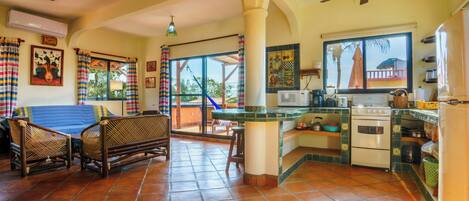 Un área de estar amplia con una mesa de comedor, sillas, un sofá, una cocina con estufa y refrigerador, y un balcón con vistas.