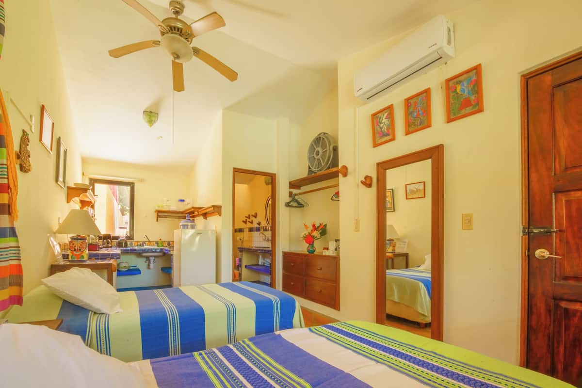 Un dormitorio con dos camas, ventilador de techo, aire acondicionado, zona de cocina y baño.